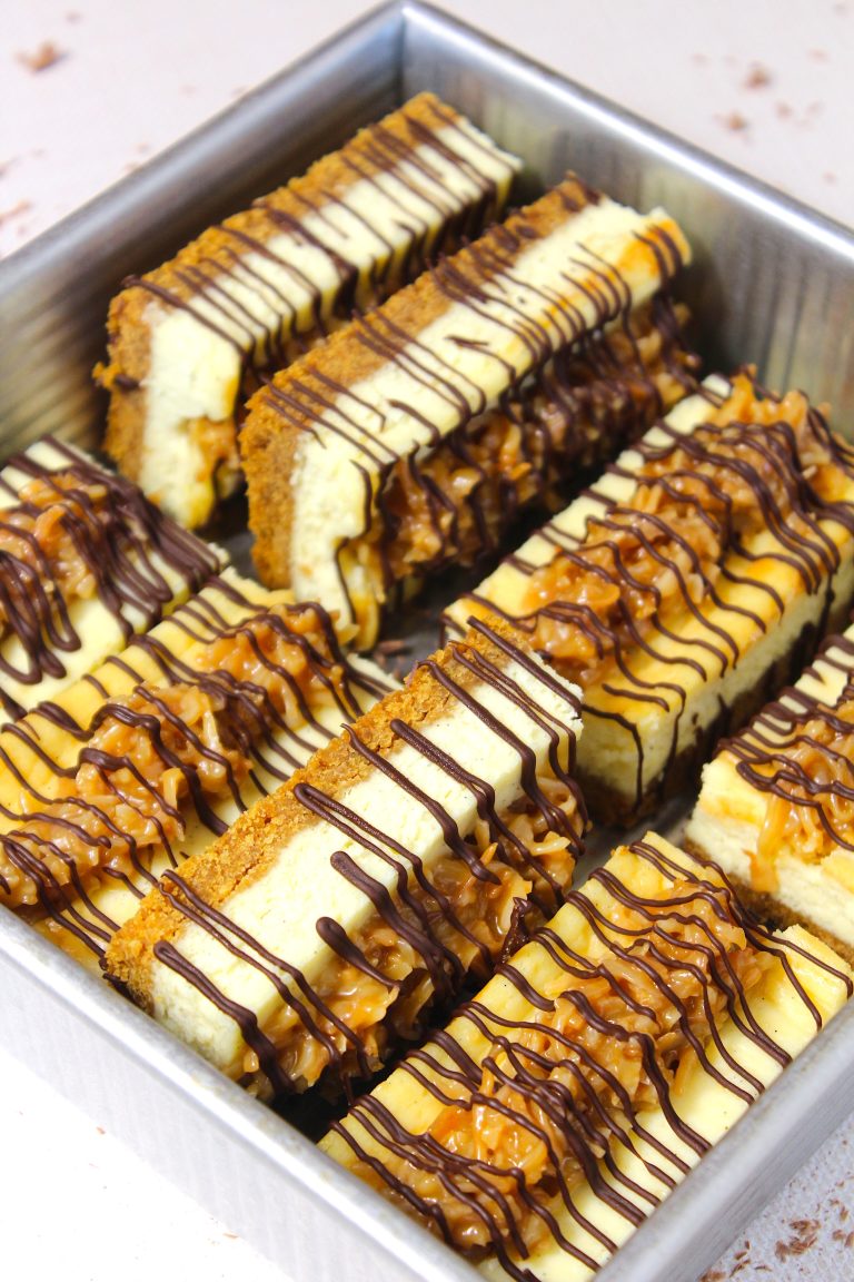 A delectable assortment of cheesecake bars drizzled with chocolate and caramel sauce, invitingly presented in a metal baking tray.