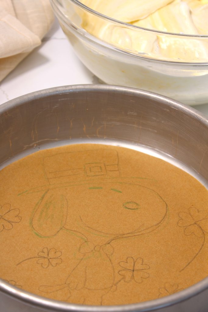 snoopy designed cake with parchment paper in pan and design traced on