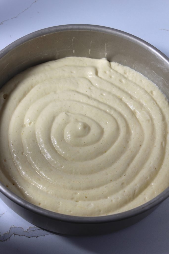 A close-up image of a creamy, smooth batter with a spiral design on top, contained in a round metal mixing bowl on a white surface.