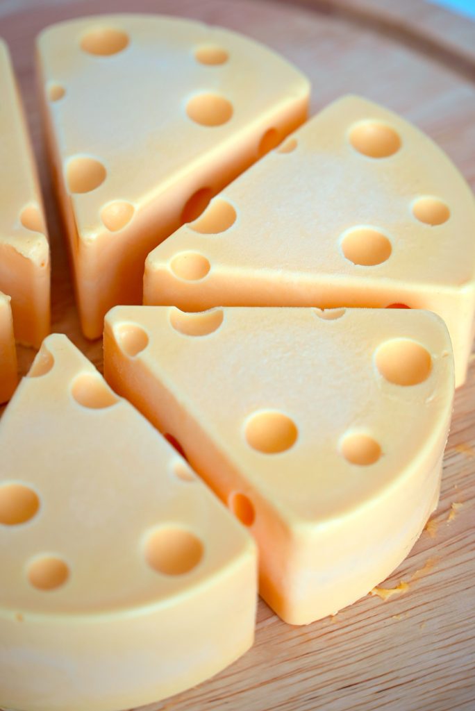 Close-up of several wedges of Swiss cheese arranged in a circle on a wooden board, showing distinctive holes and smooth yellow surfaces.
