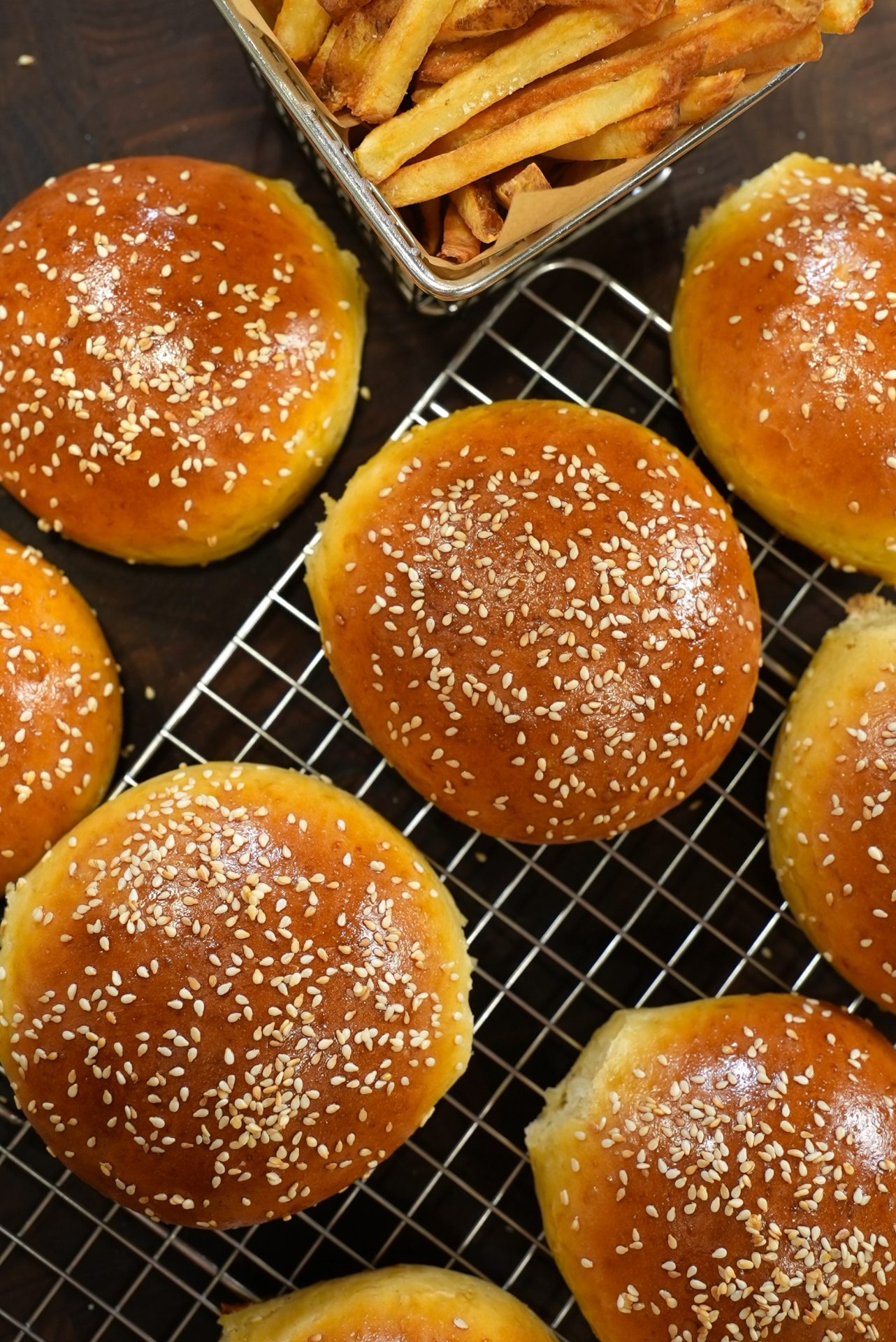 Golden brown sesame seed hamburger buns cooling on a wire rack with a container of golden french fries in the corner.